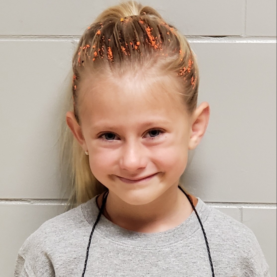 smiling girl with blonde hair wearing a gray sweatshirt with orange sparkles in her hair