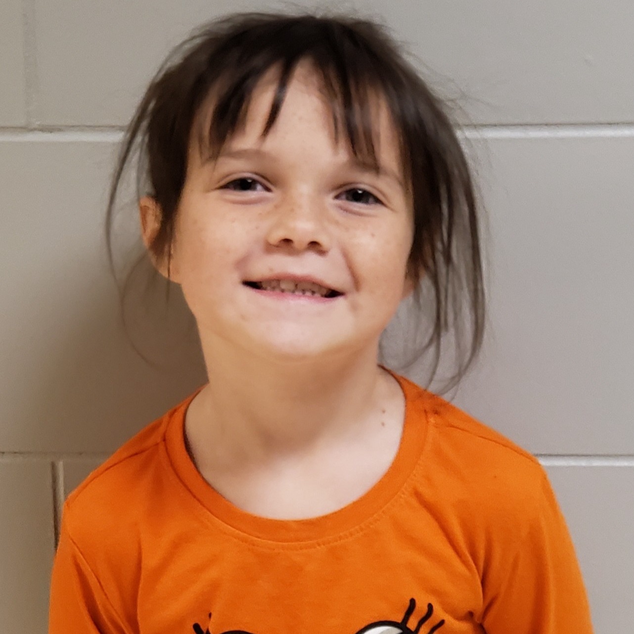 smiling girl with dark hair pulled up wearing an orange t-shirt