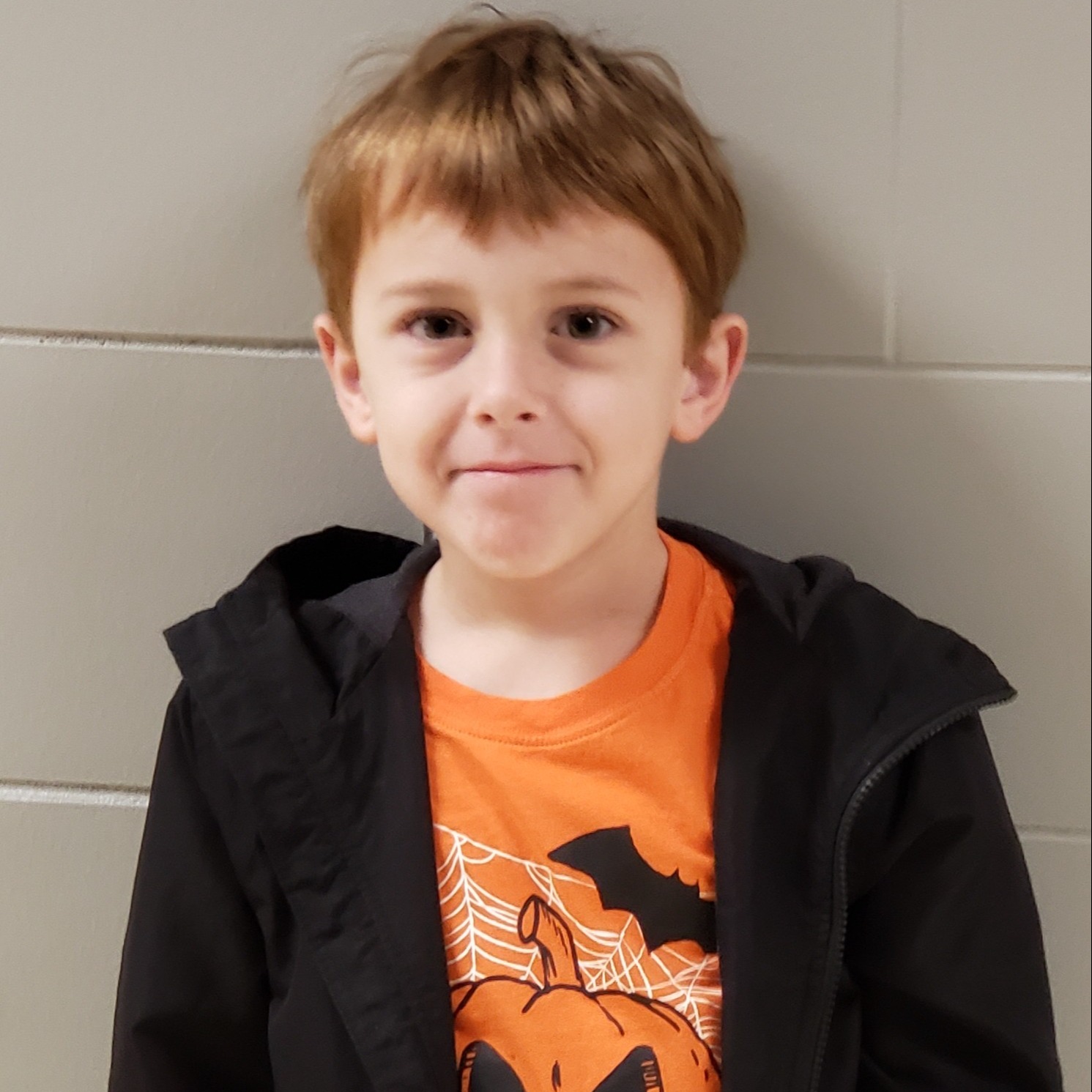 boy with red hair wearing an orange Halloween t-shirt under a black jacket