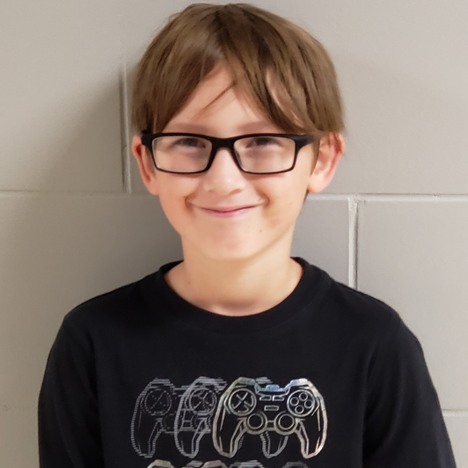 smiling boy with light brown hair and black-rimmed glasses wearing a black t-shirt