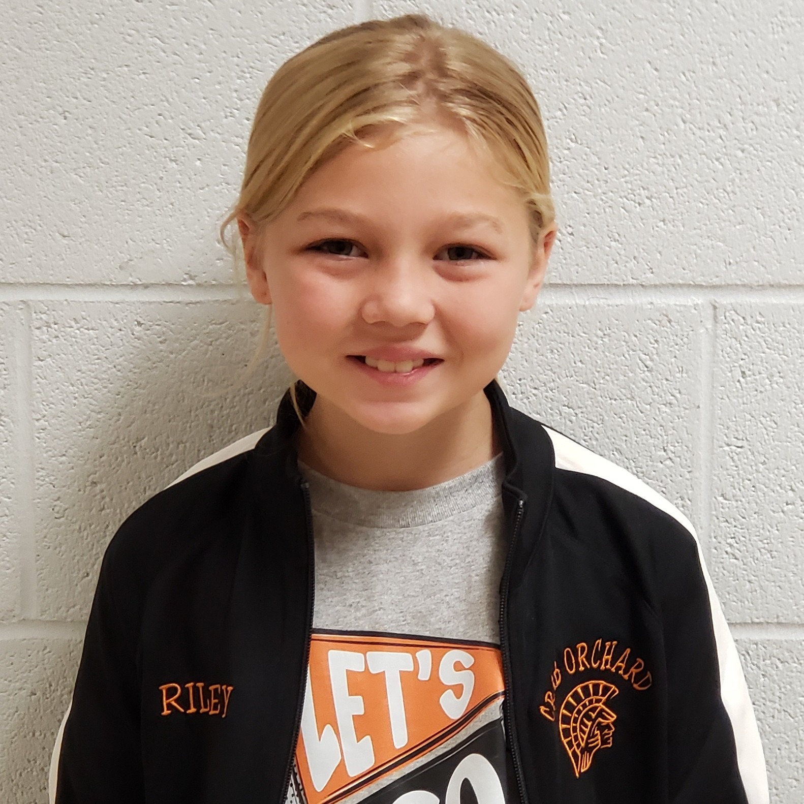 smiling girl with blonde hair pulled back wearing a gray t-shirt under a black & white jacket