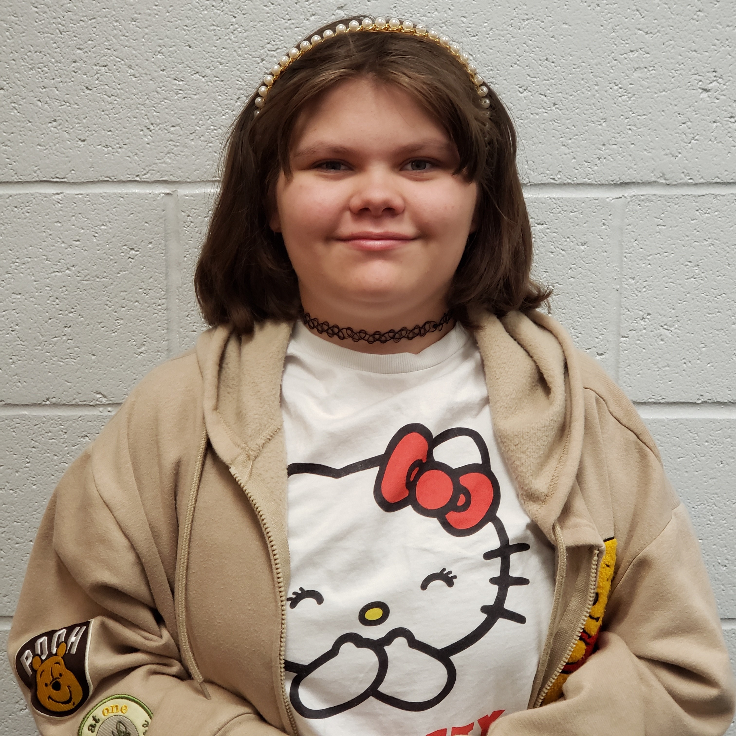 smiling girl with dark hair in a pear headband wearing a Hello Kitty t-shirt under a tan jacket