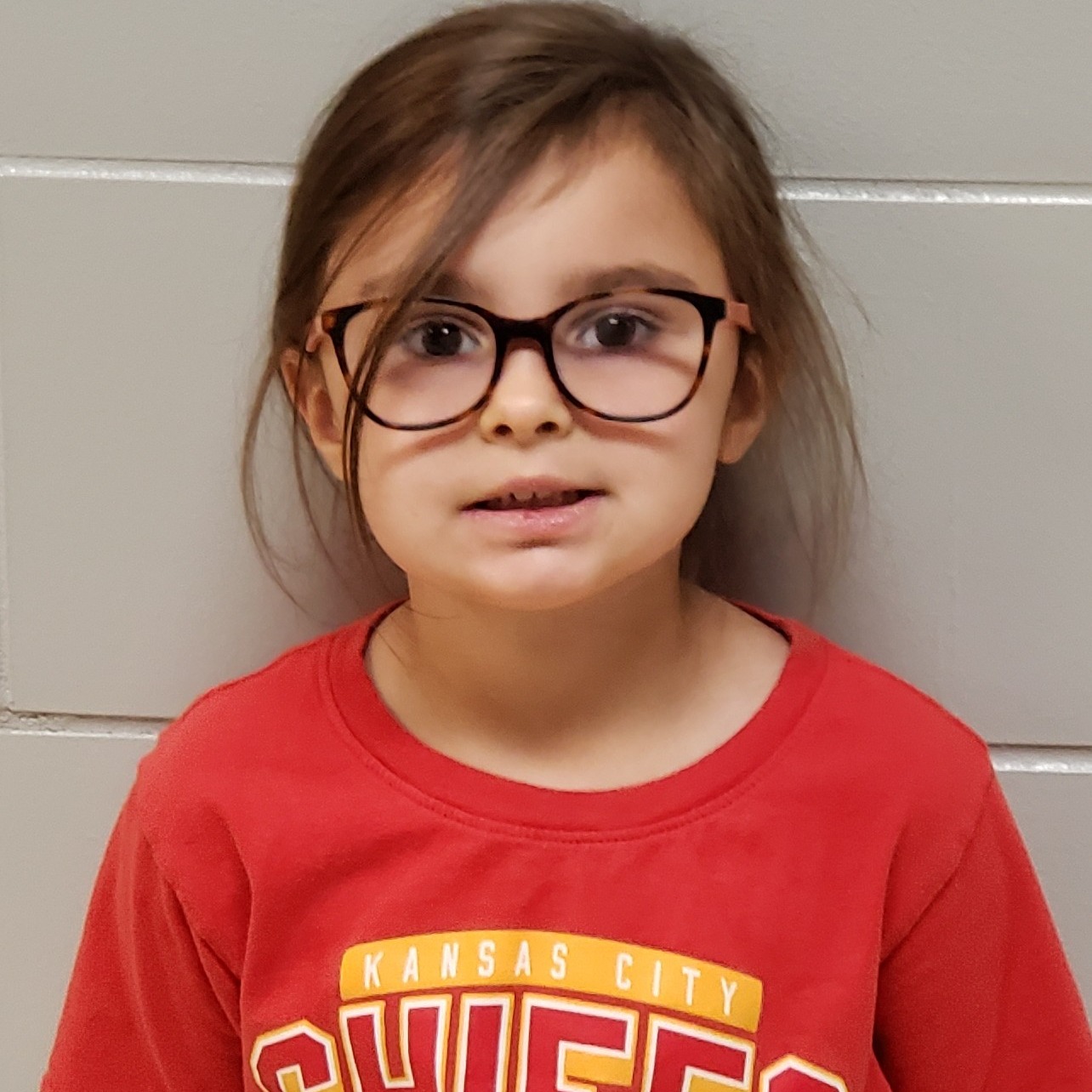 young girl with dark hair pulled back & glasses wearing a red t-shirt