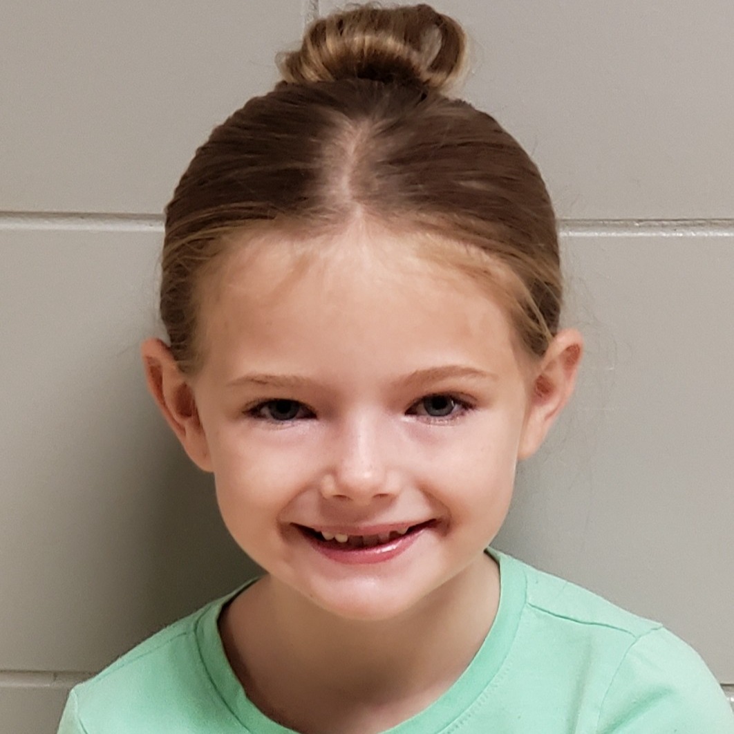 smiling young girl with dark blonde hair pulled up in a bun wearing a mint green t-shirt
