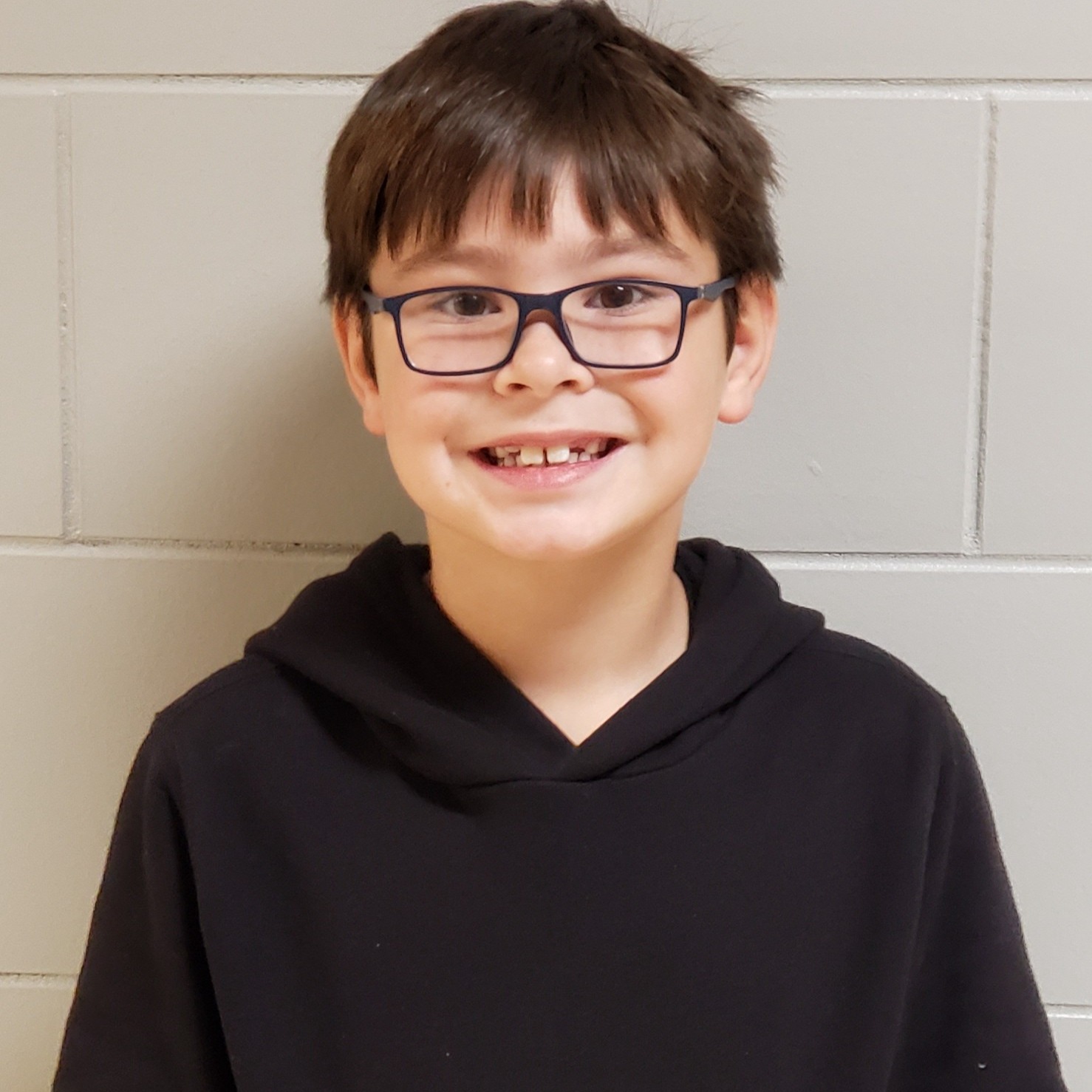 smiling young boy with dark hair and glasses wearing a black hoodie