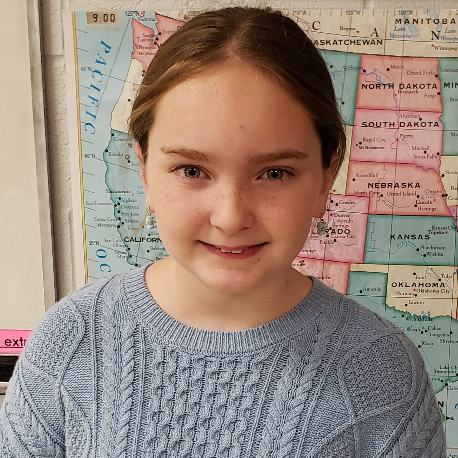 smiling girl with reddish brown hair and freckles wearing a light blue sweater