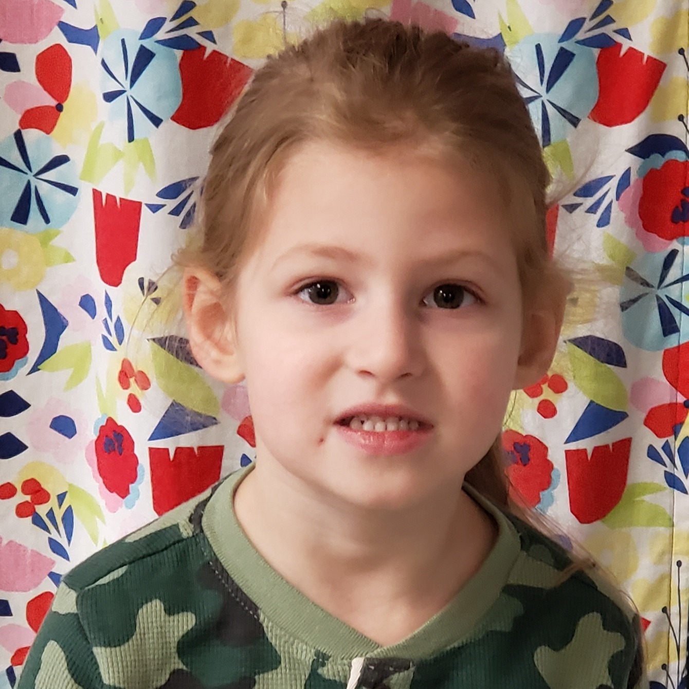 young girl with light brown hair pulled back wearing a camouflage shirt