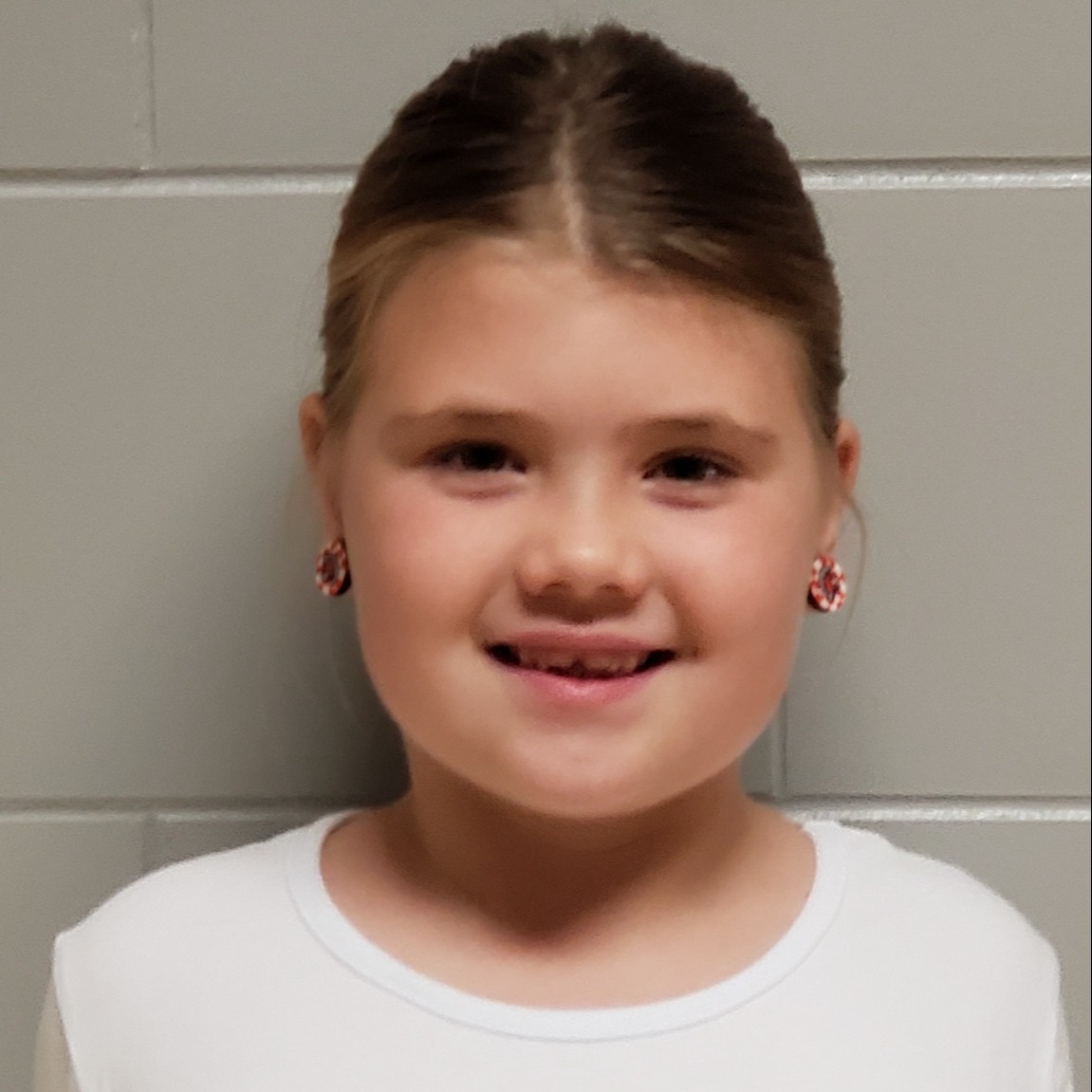 smiling girl with dark blonde hair wearing a red & white earrings and a white shirt