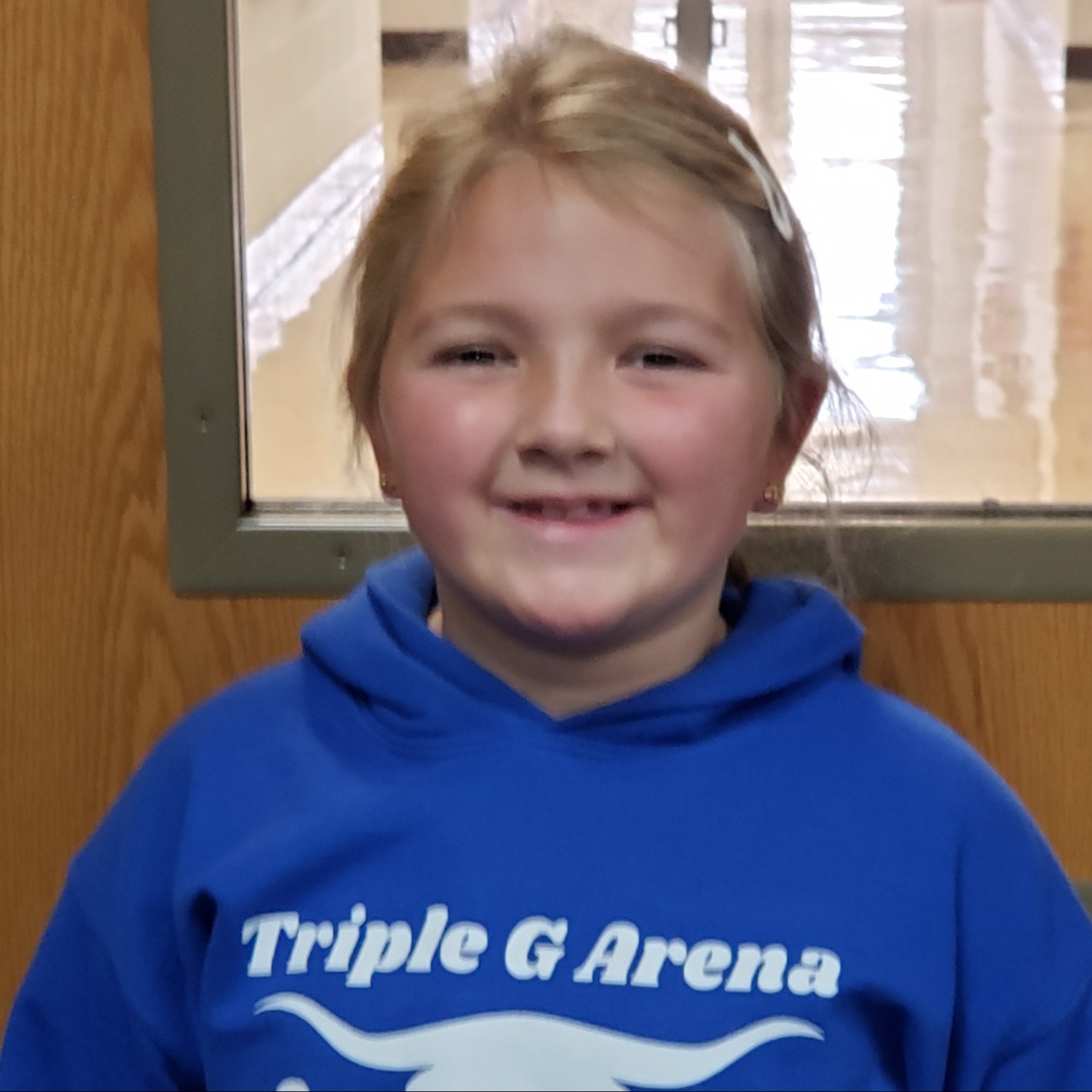 smiling young girl with blonde hair pulled back wearing a blue hoodie