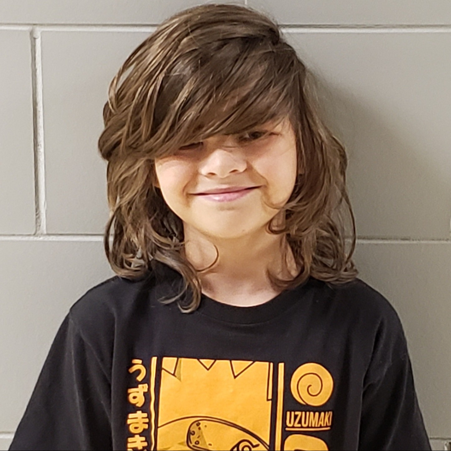 smiling boy with long brown hair over his face wearing a black & yellow  t-shirt