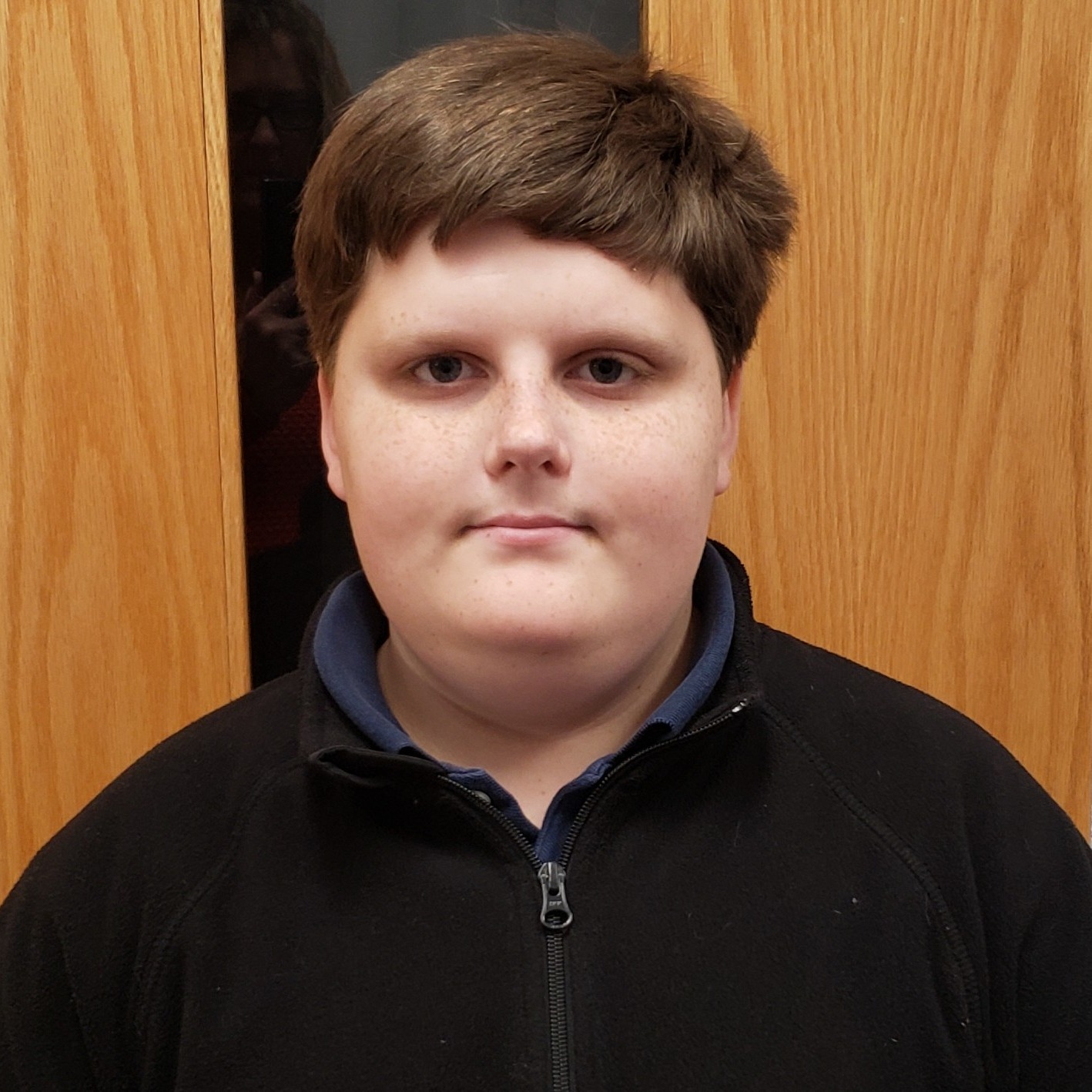 boy with brown hair wearing a navy polo under a black zipped-up jacket