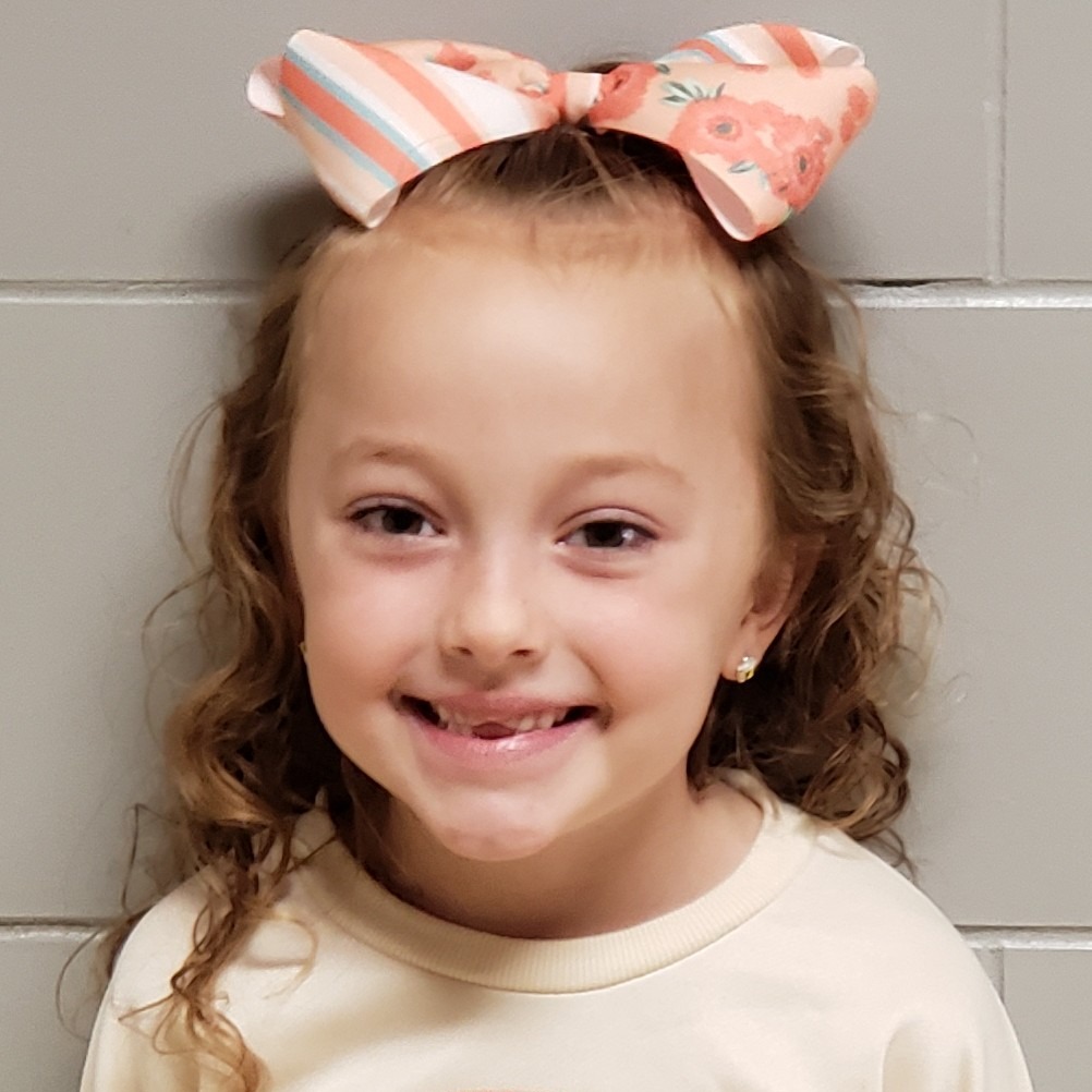 smiling girl with reddish hair wearing a large peach bow and a cream sweatshirt