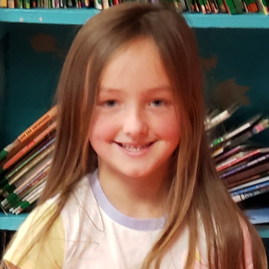 smiling young girl with brown hair wearing a white t-shirt with yellow sleeves and blue collar