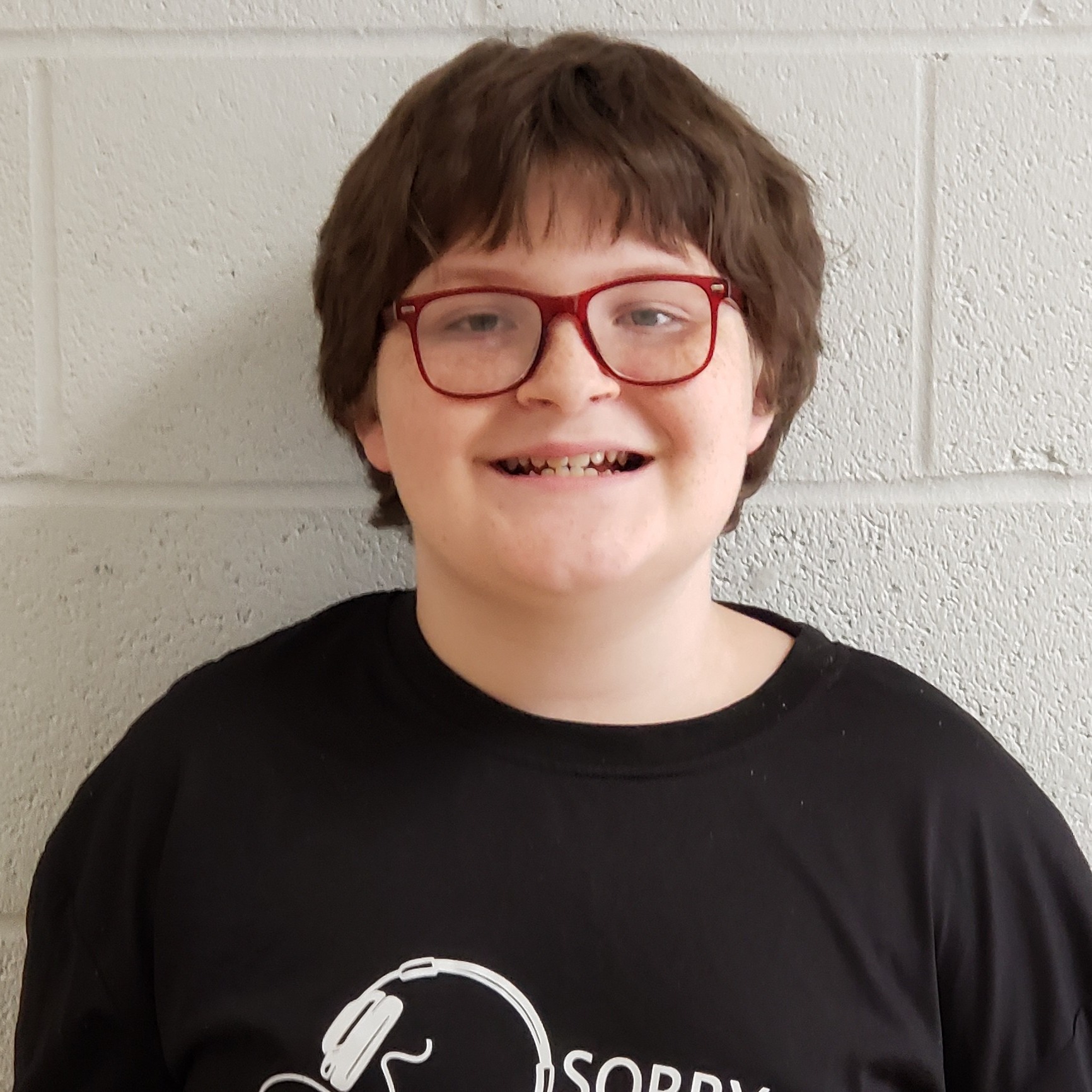 smiling boy with brown hair and red glasses wearing a black t-shirt