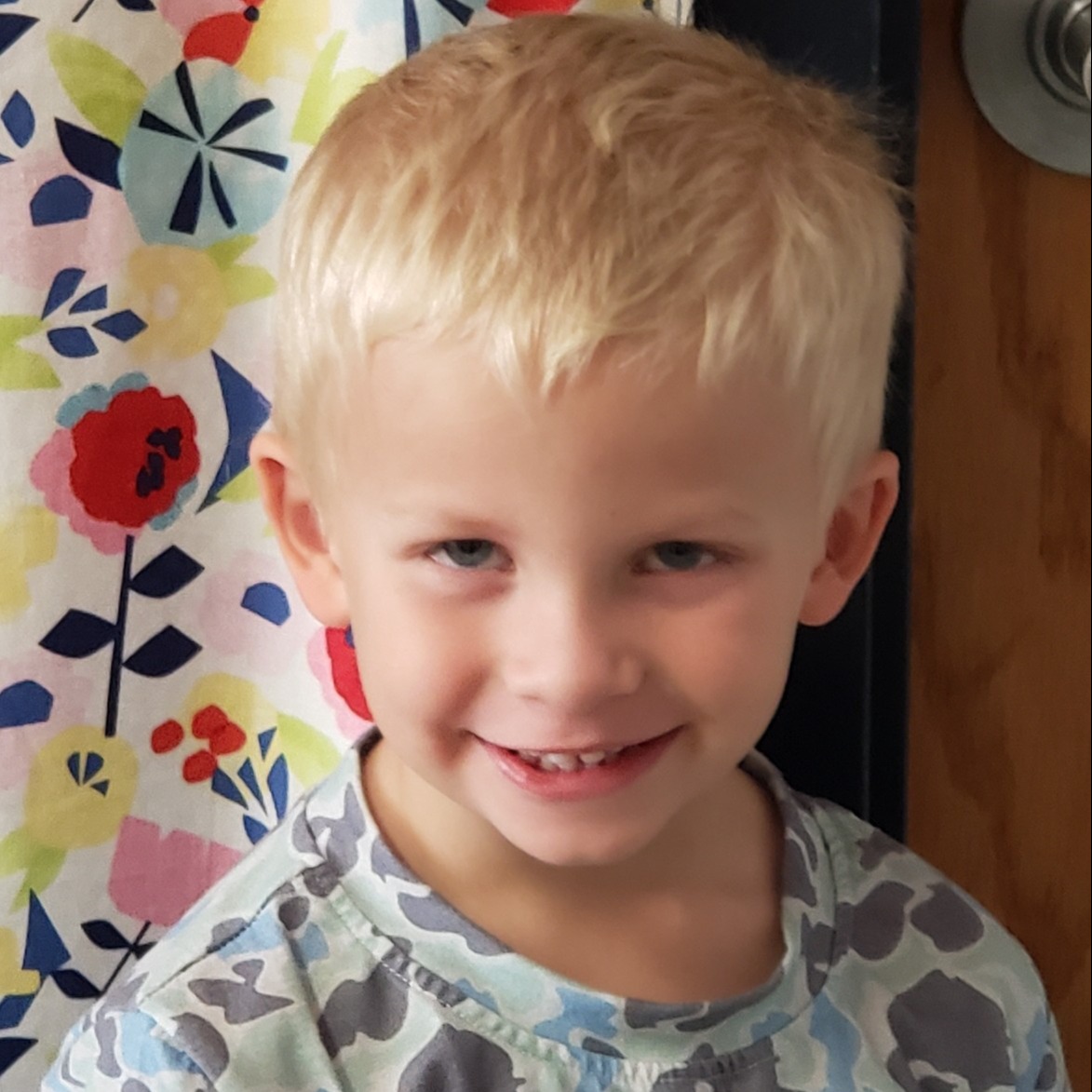 smiling little boy with blonde hair wearing a camouflage shirt