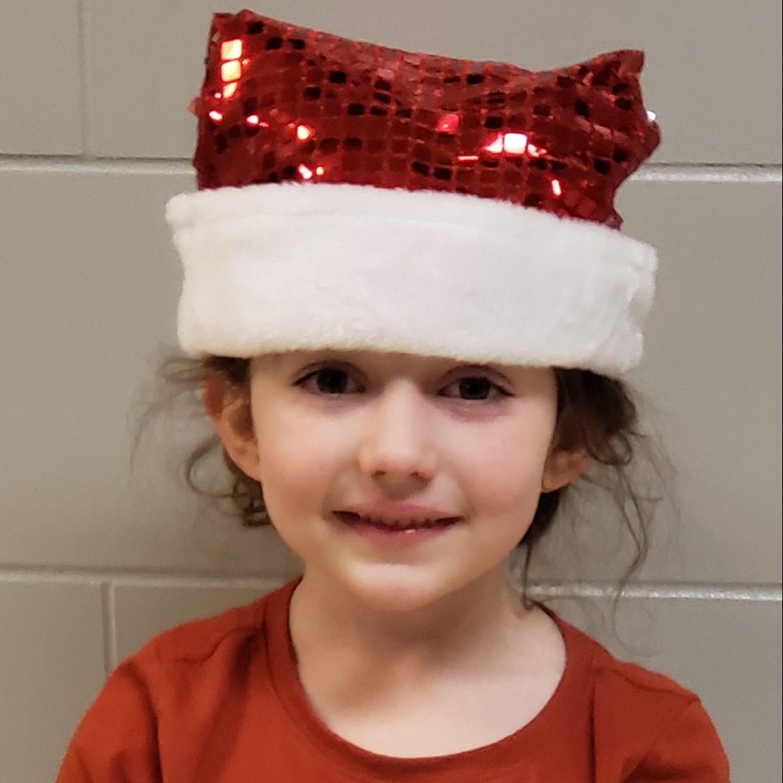 smiling little girl with dark hair wearing a red,sparkly Santa hat and a red t-shirt
