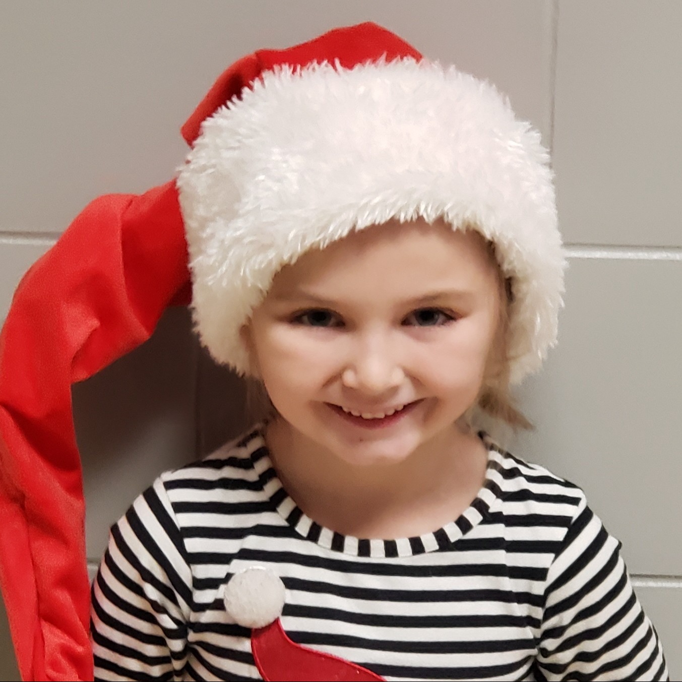smiling girl with blonde hair wearing a Santa hat and a black-&-white striped shirt