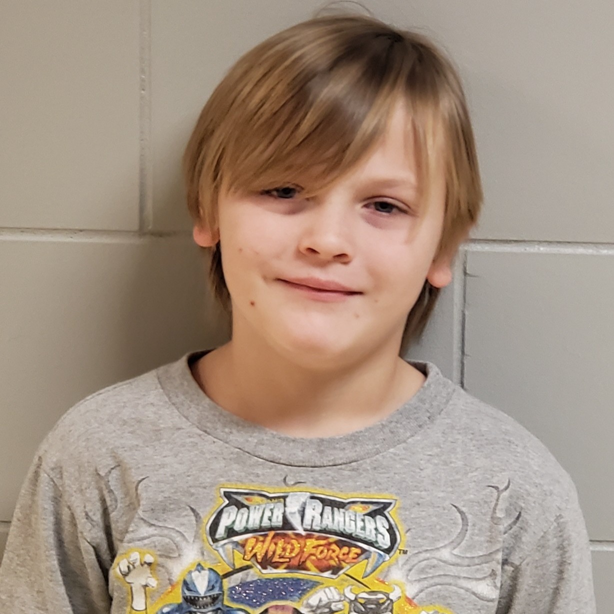 grinning boy with blonde hair wearing a gray power rangers t-shirt