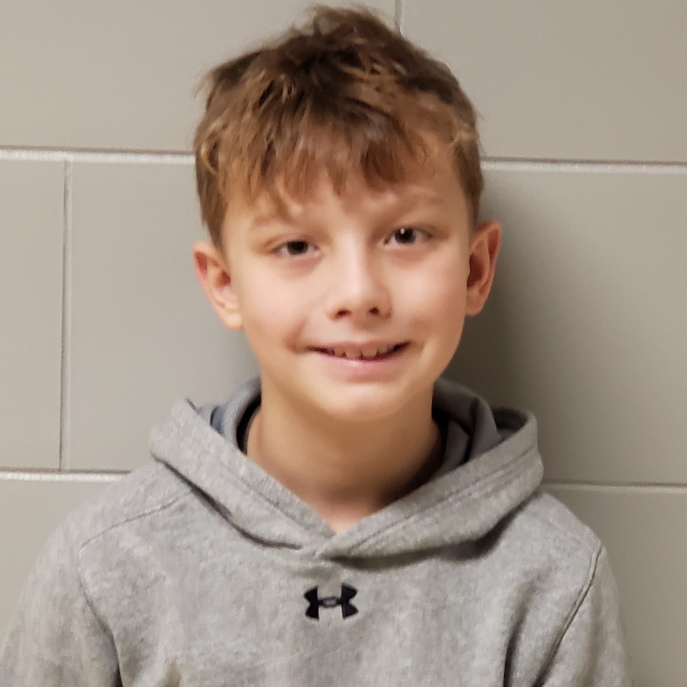 smiling boy with dark blonde hair wearing a gray hoodie