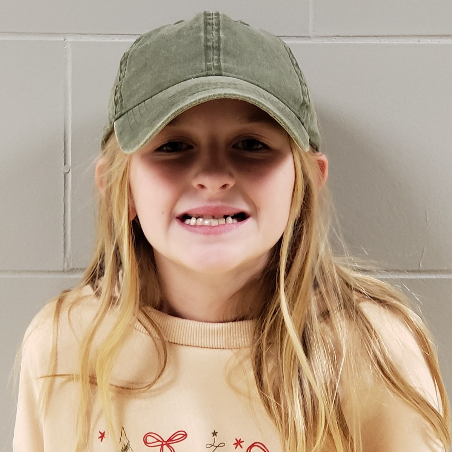 smiling girl with blonde hair wearing a green cap and yellow sweatshirt