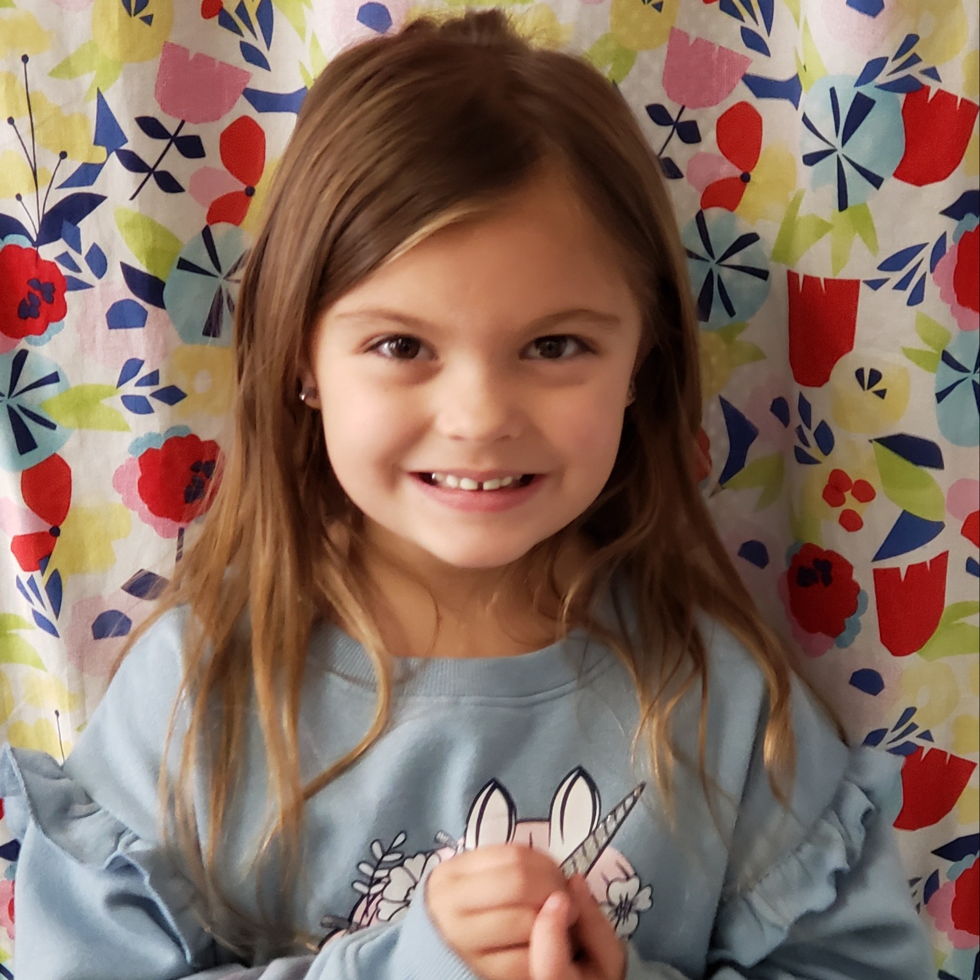 smiling little girl with light brown hair wearing a light blue sweatshirt with ruffles and a unicorn