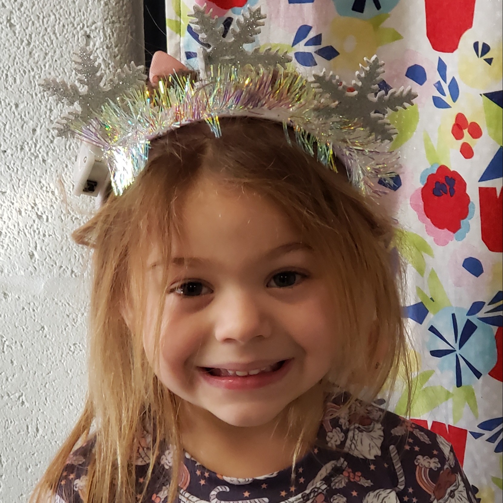 smiling little girl with light brown hair wearing a snowflake headband and a navy dress with Santa & candy canes on it