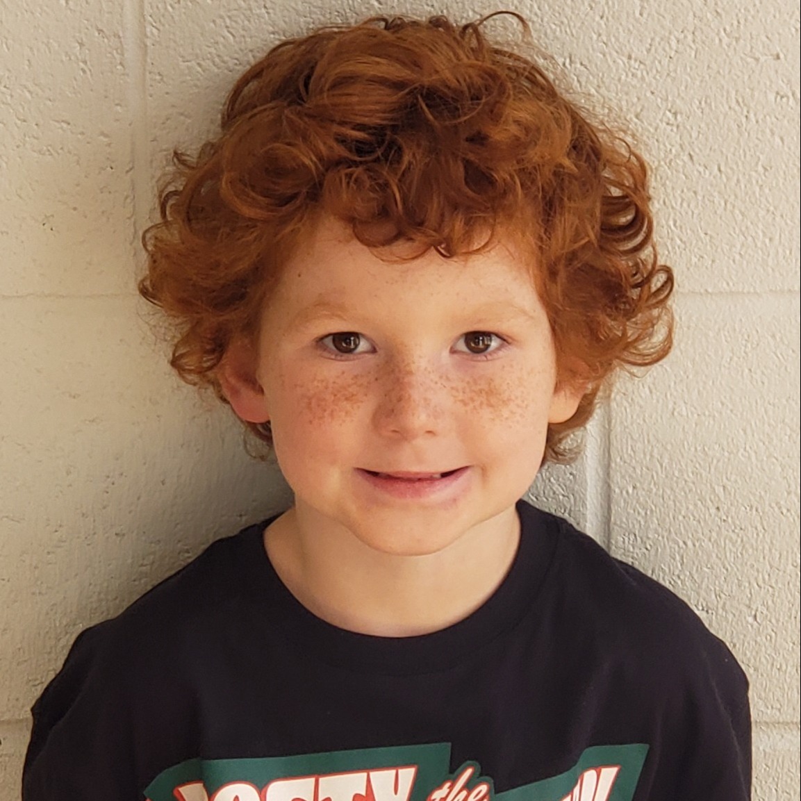 smiling little boy with red curly hair and freckles wearing a black t-shirt