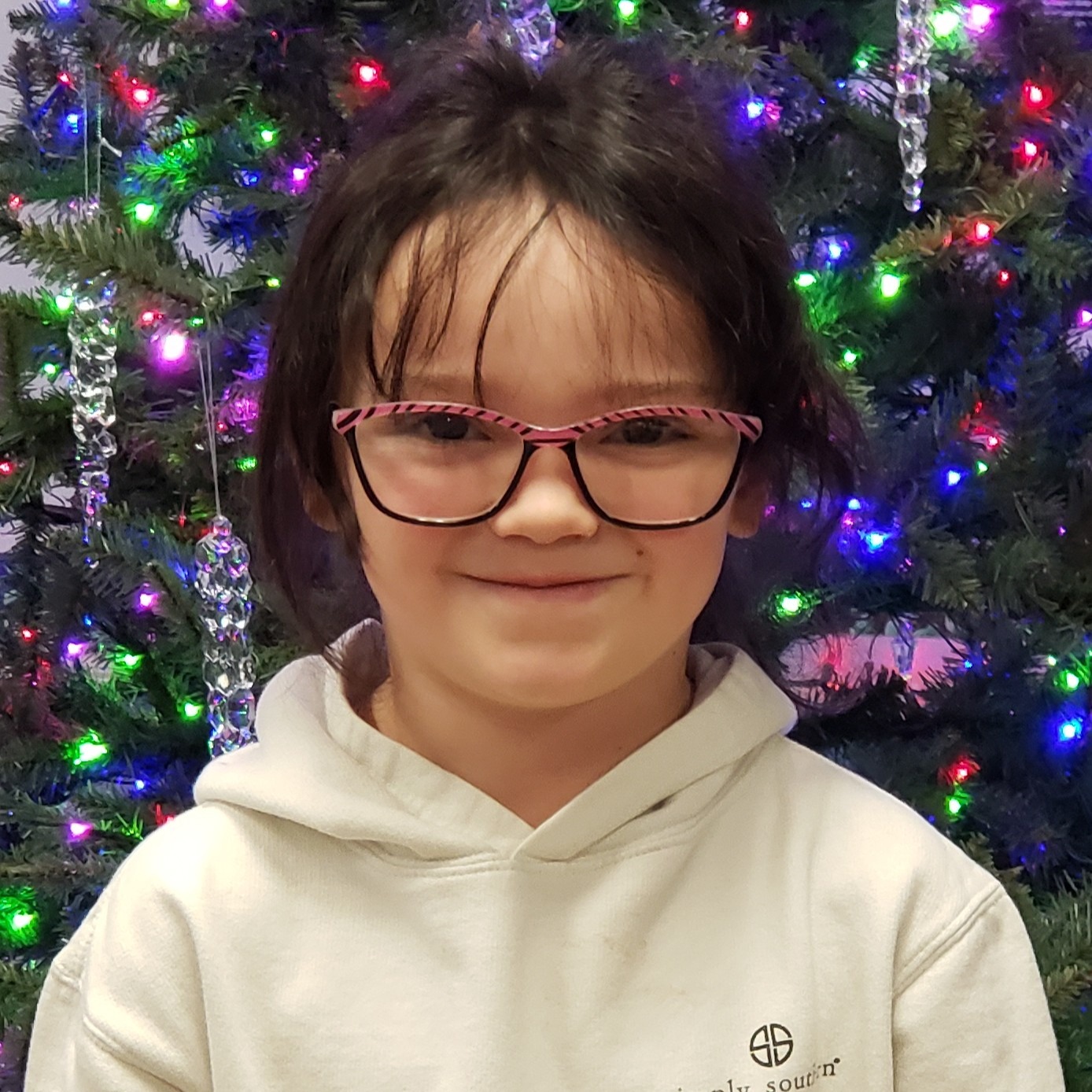 smiling girl with black hair pulled back wearing glasses and a cream hoodie