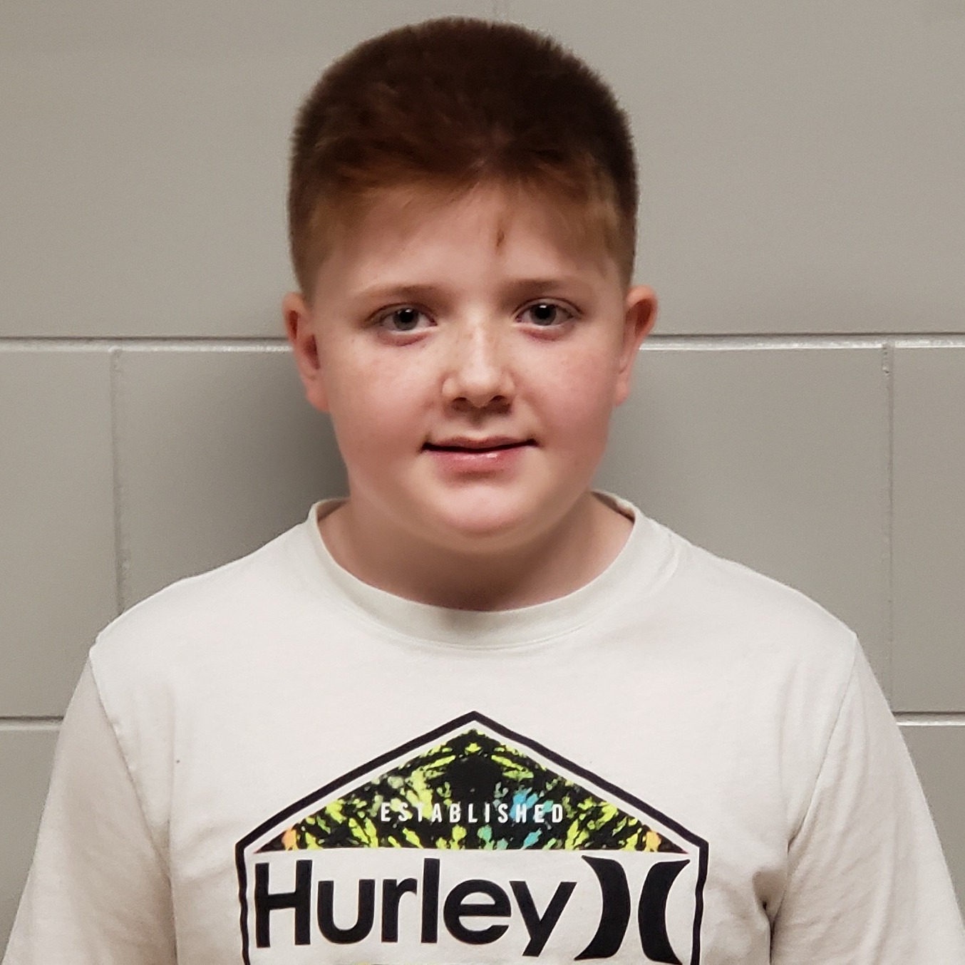 grinning boy with spiky reddish hair and freckles wearing a white Hurley t-shirt