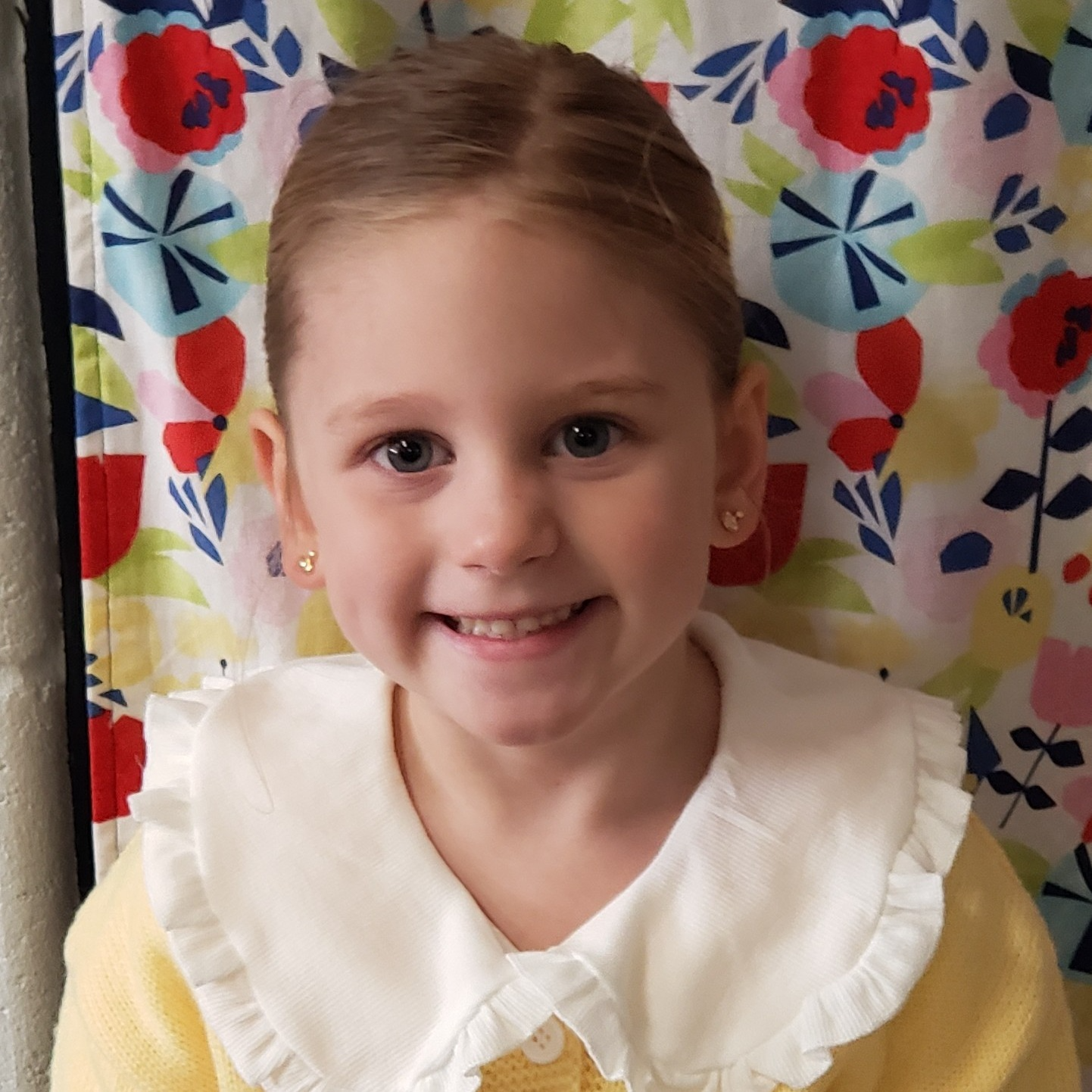 smiling little girl with blonde hair pulled back wearing a light yellow sweater with a large white collar