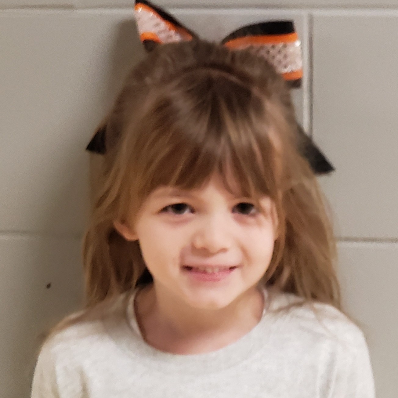 smiling girl with brown hair pulled half up in an orange & black bow wearing a gray t-shirt