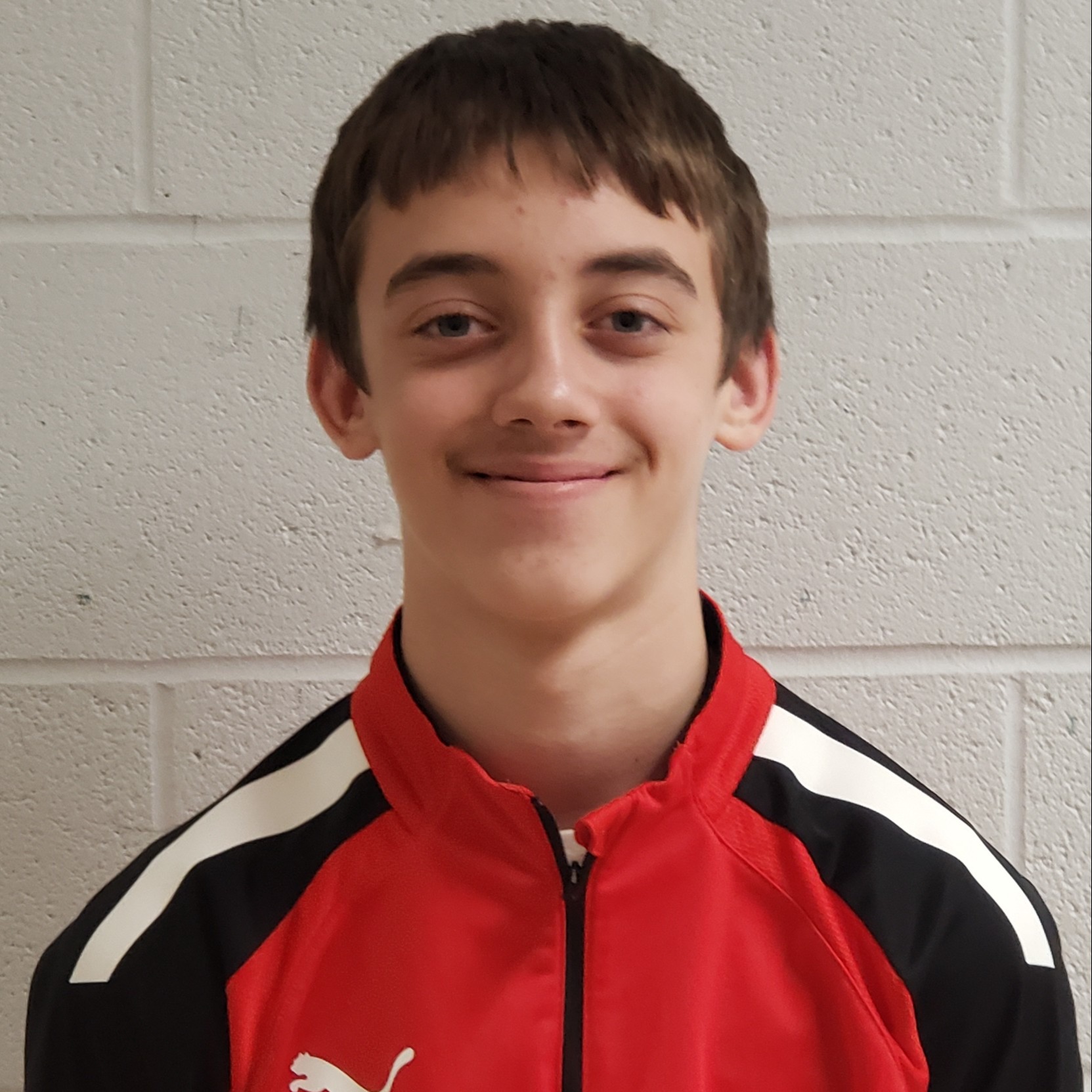 grinning boy with brown hair wearing a red, black, & white jacket zipped up