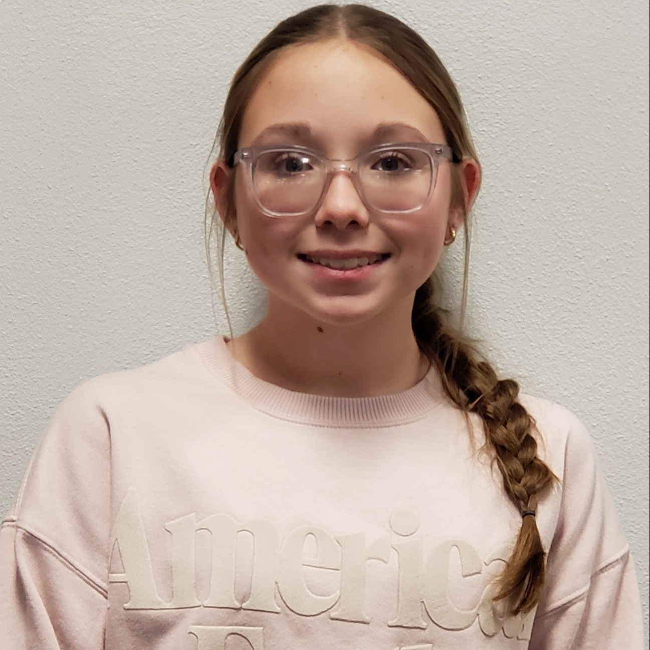 smiling girl with brown hair pulled back in a braid wearing glasses and a pink sweatshirt