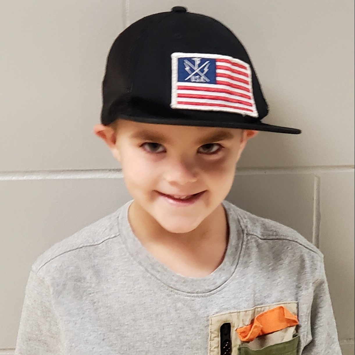 smiling little boy wearing a black hat with a flag on it and a gray t-shirt