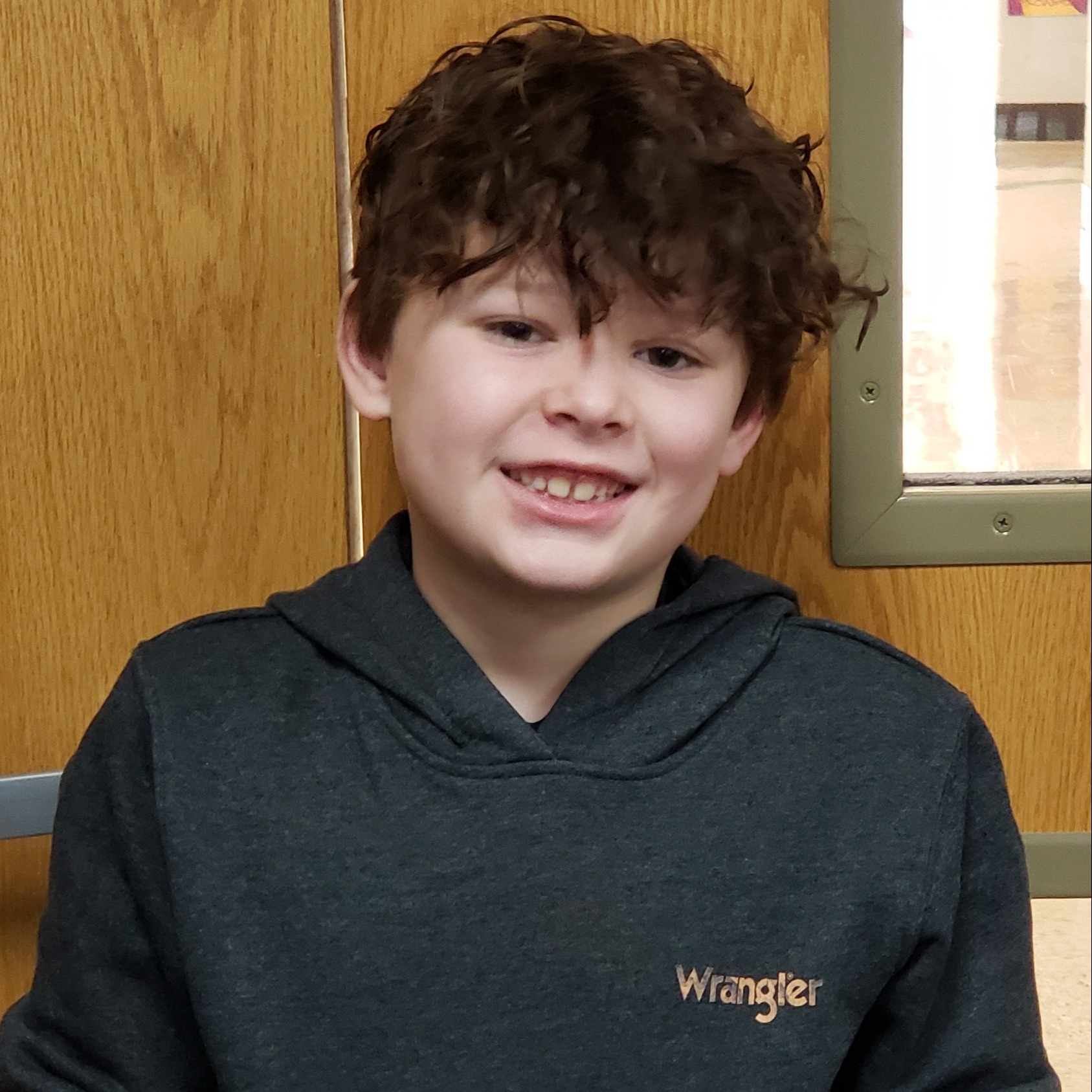 smiling boy with dark hair wearing a dark gray Wrangler hoodie