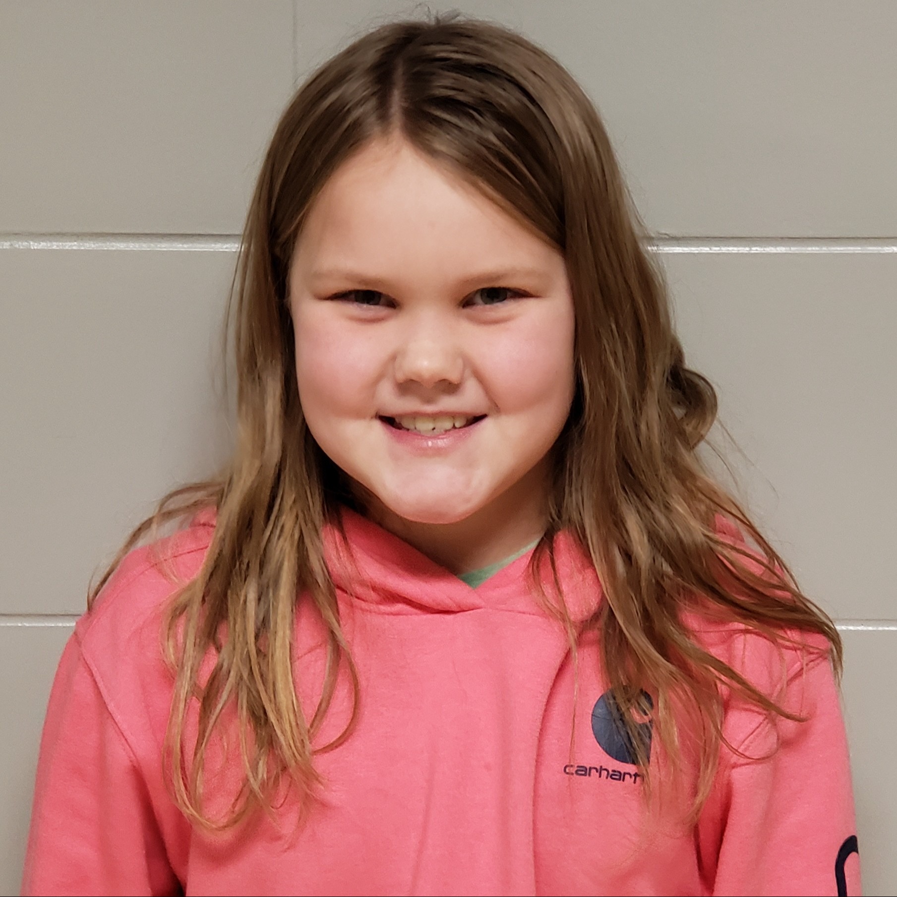 smiling girl with light  brown hair wearing a pink hoodie