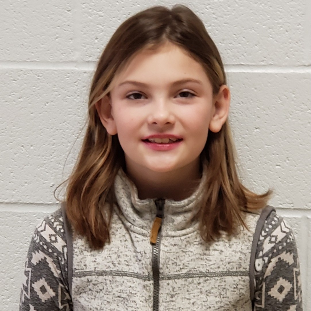 smiling girl with dark blonde hair wearing a gray vest zipped up over a gray & white shirt