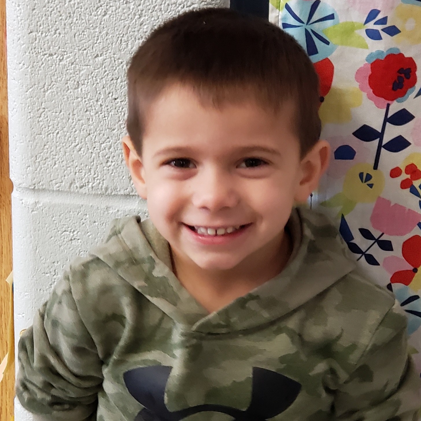 smiling little boy with dark hair wearing a camouflage hoodie