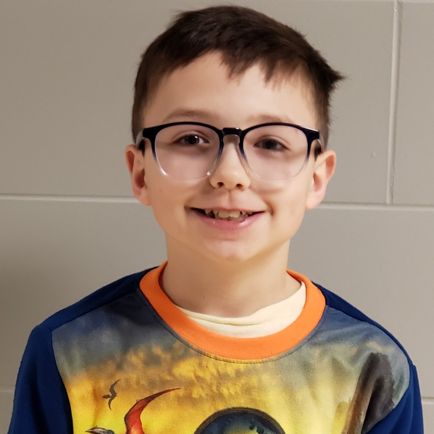 smiling boy with dark hair and glasses wearing Jurassic World pajamas