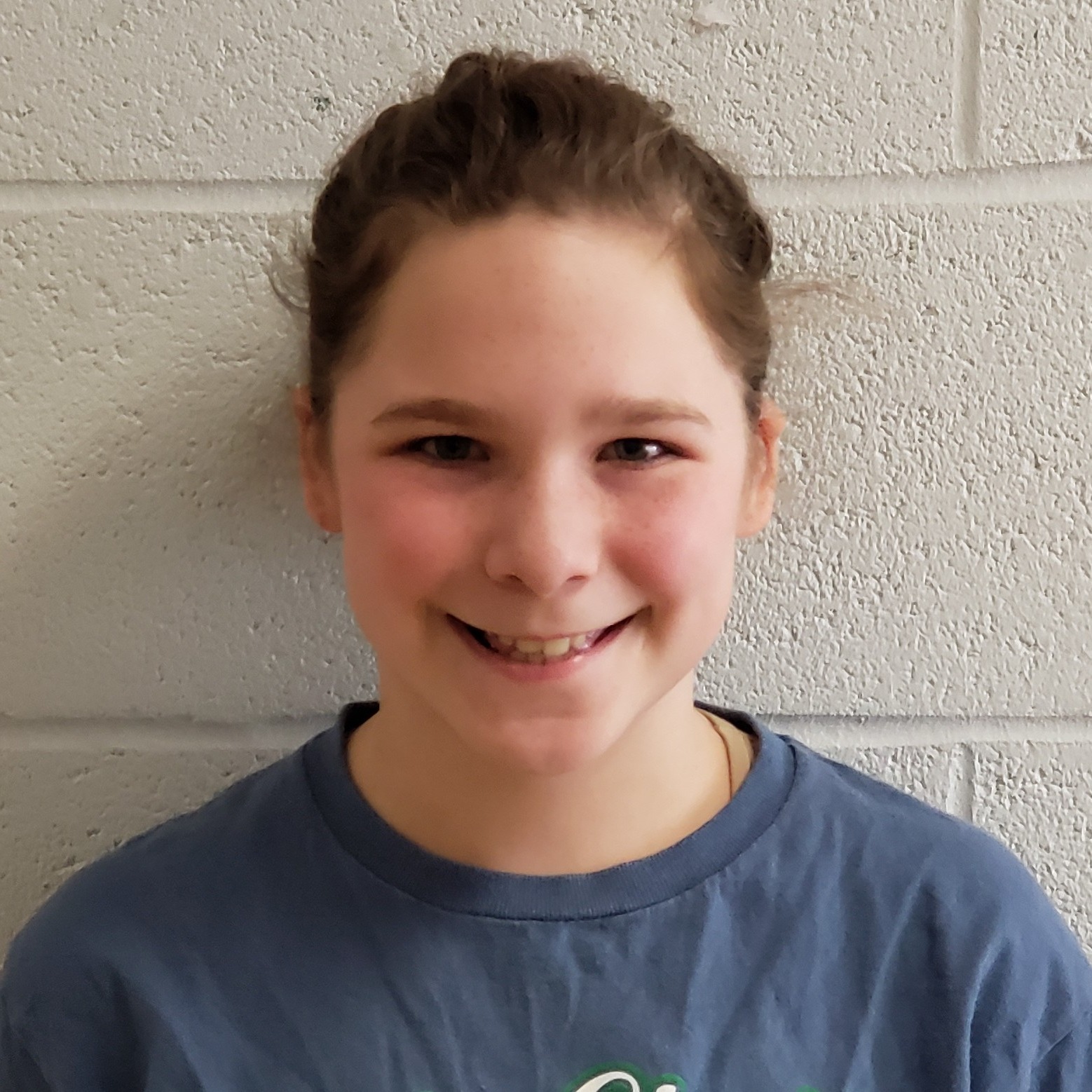 smiling girl with light brown hair pulled back wearing a blue t-shirt