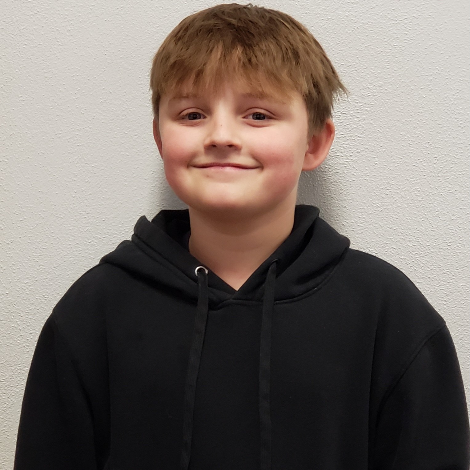grinning boy with light brown hair wearing a black hoodie