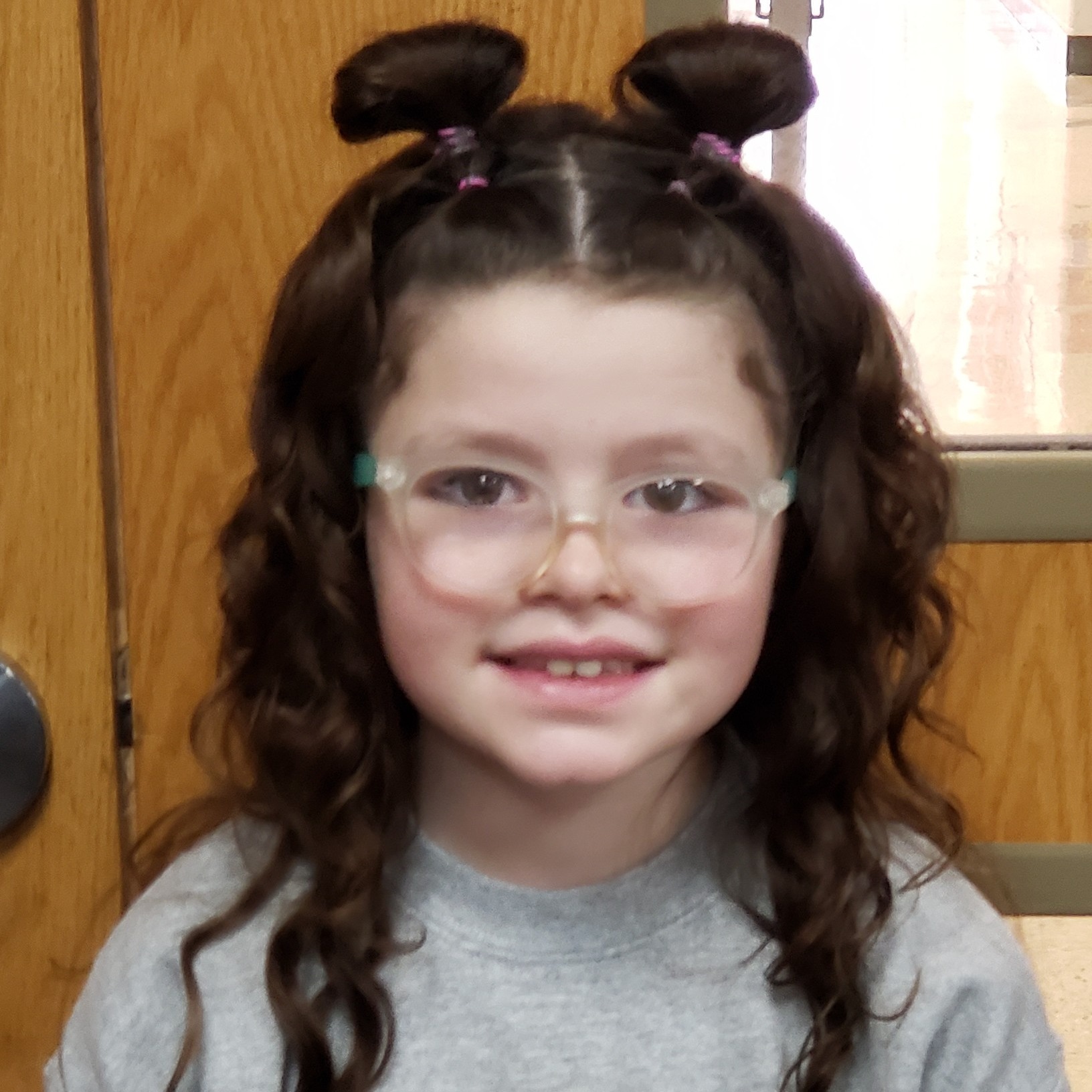 smiling girl with dark hair pulled half up in alien buns wearing glasses and a gray sweatshirt