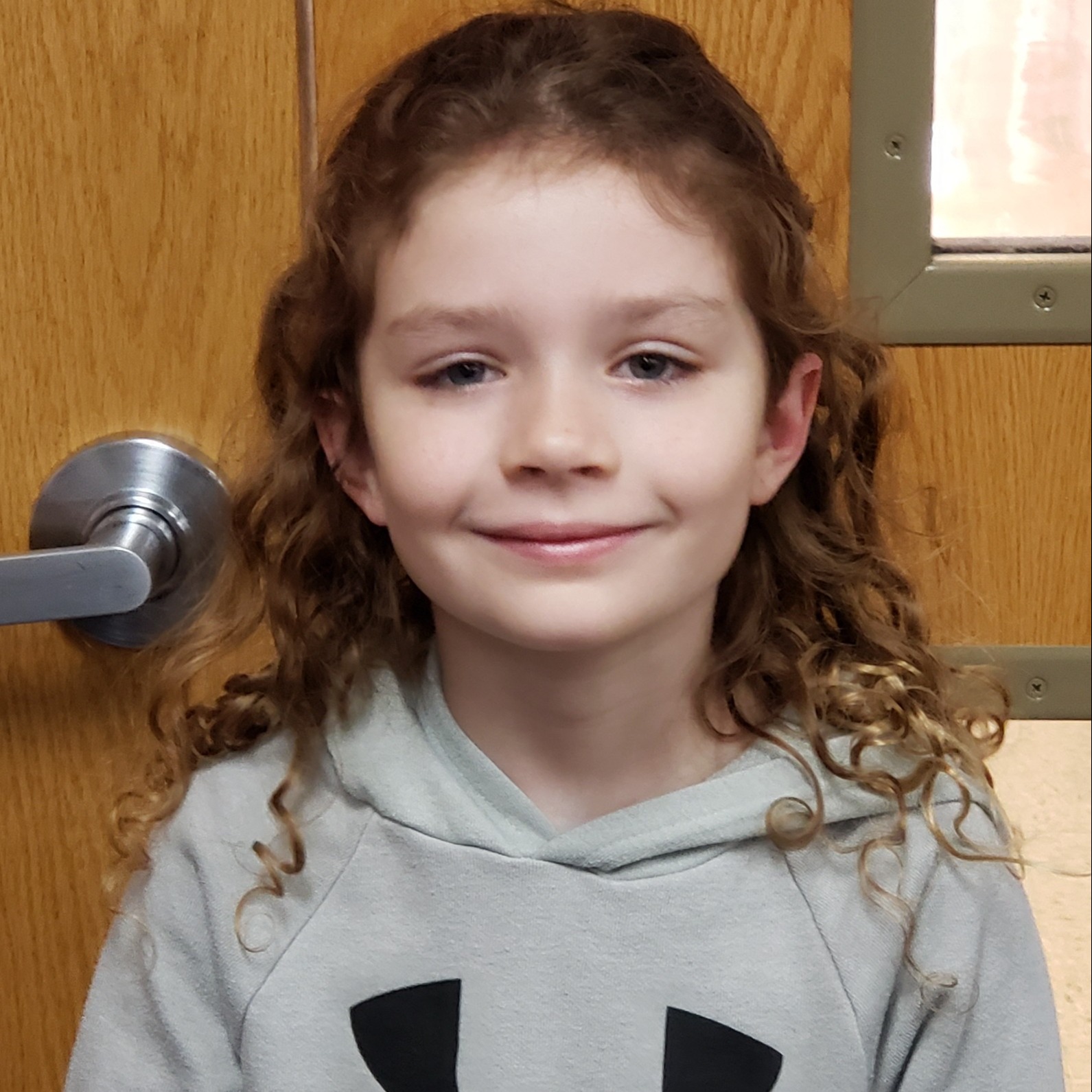smiling girl with long curly brown hair wearing a gray hoodie