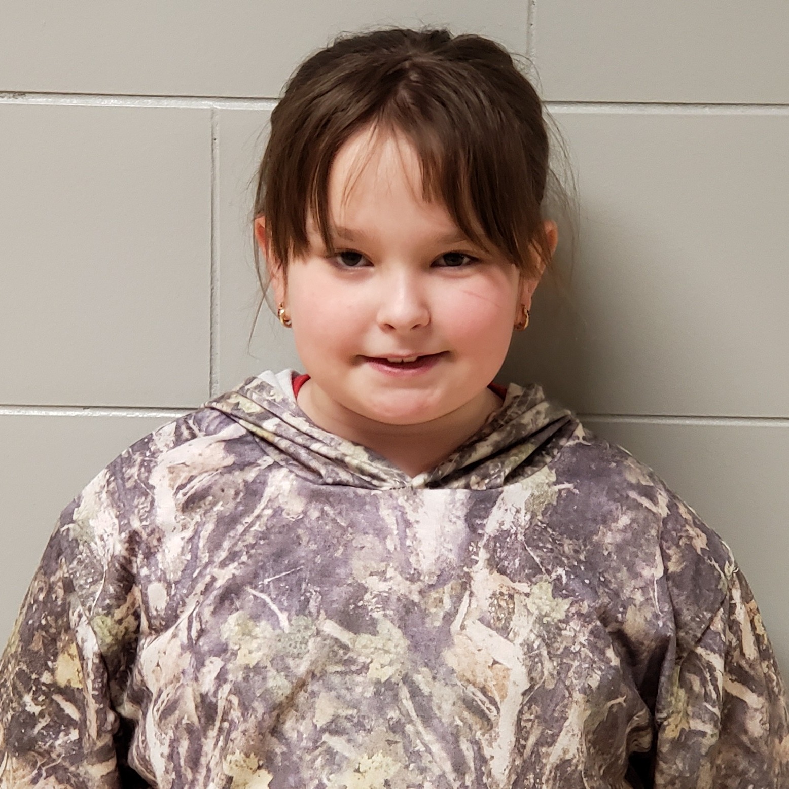 smiling girl with dark hair pulled back wearing a camouflage hoodie