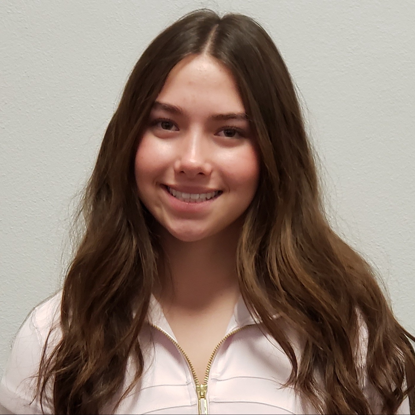 smiling young lady with long brown hair wearing a pink  3/4 zip shirt