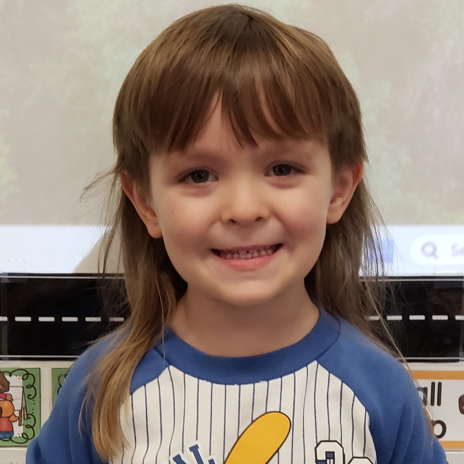 smiling little boy with light brown mullet wearing a blue & white baseball jersey