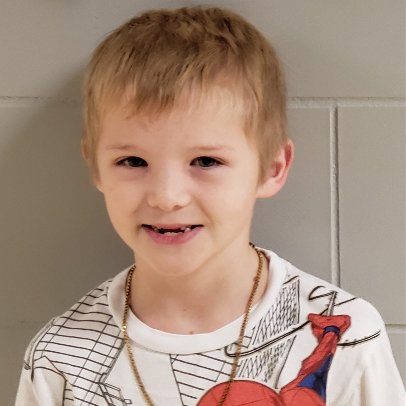 smiling boy with blonde hair wearing a white spiderman t-shirt