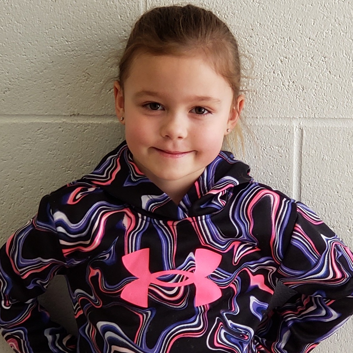 grinning young girl with brown hair pulled back wearing a black hoodie with purple, white, & pink swirls