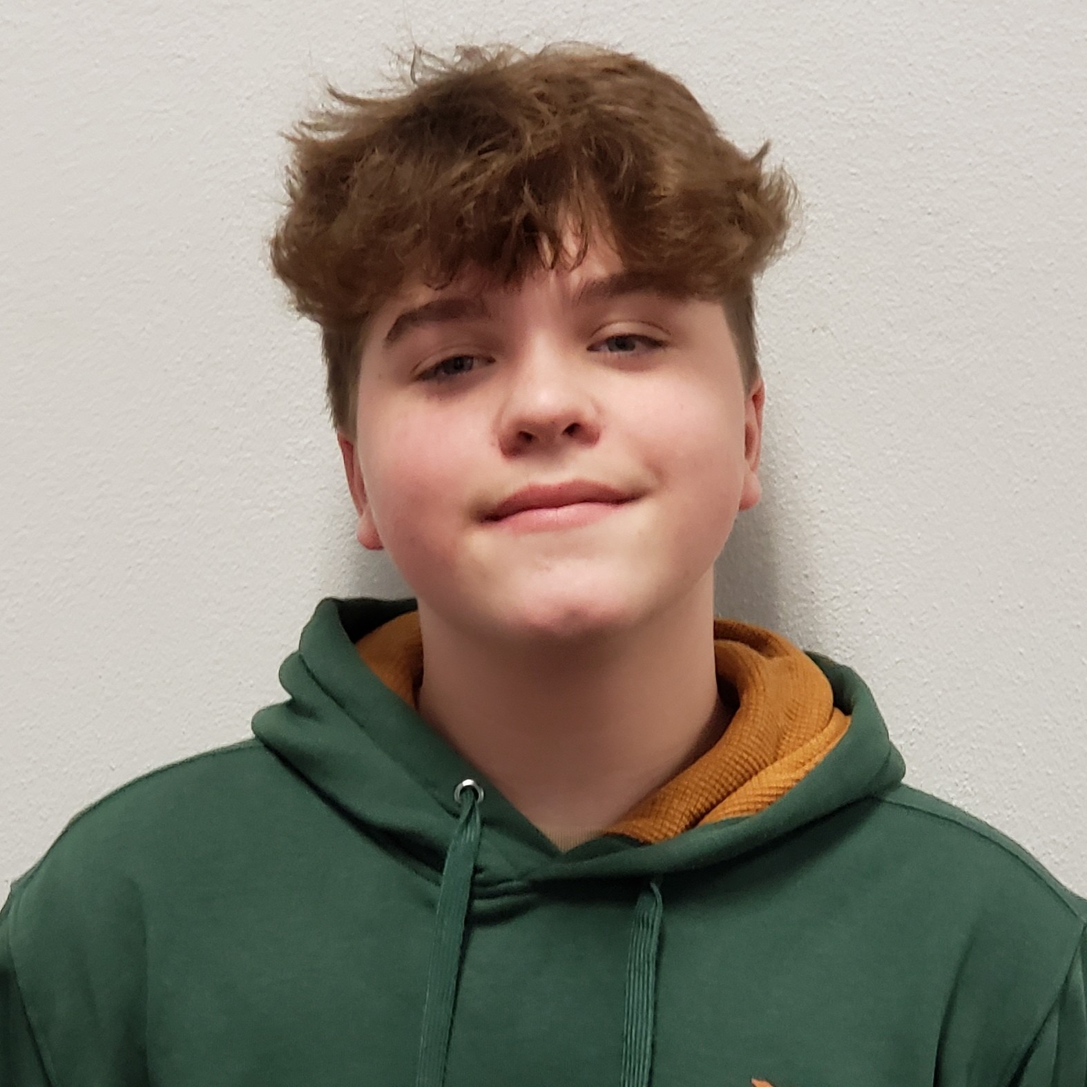 grinning boy with brown hair wearing a green hoodie