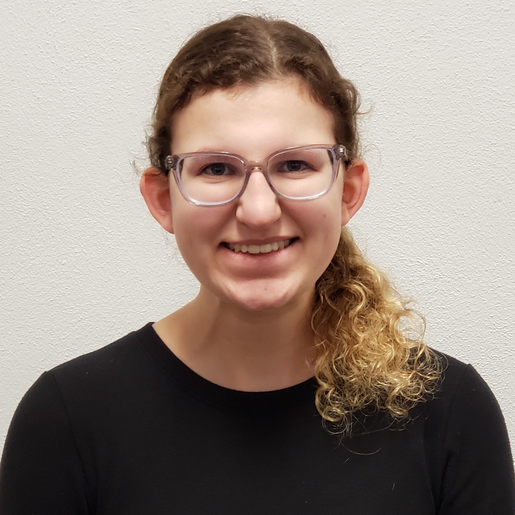 smiling young lady with curly blonde hair pulled back wearing a black t-shirt and glasses